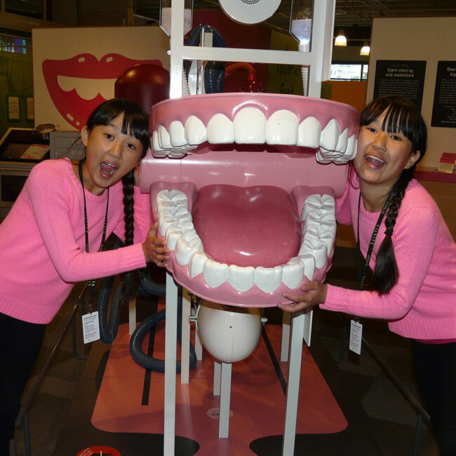 Twin Sisters Mia and Alexandra in a museum with giant wind-up teeth.