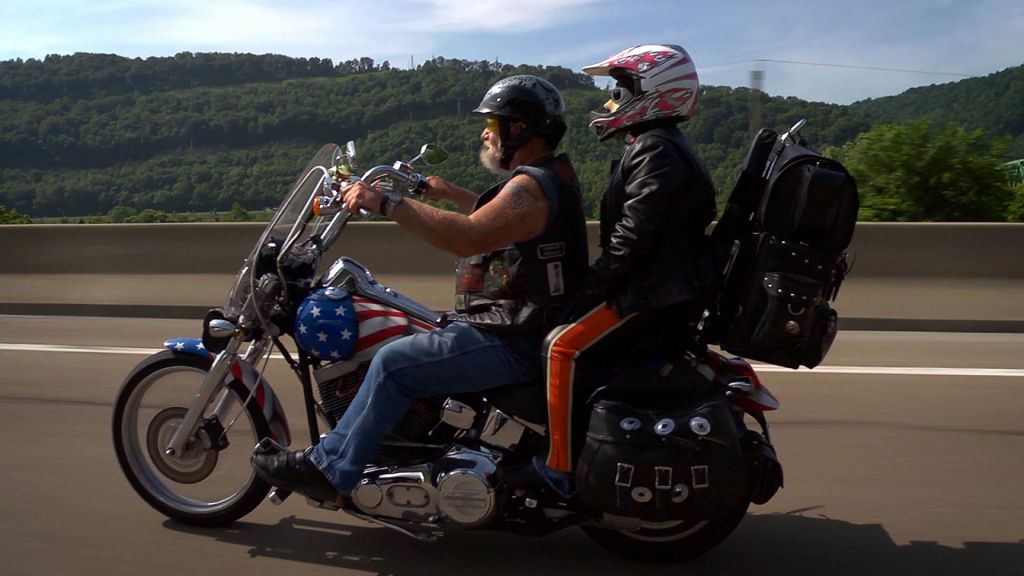 Ron "Stray Dog" Hall and his wife ride their American flag Harley along a country highway.