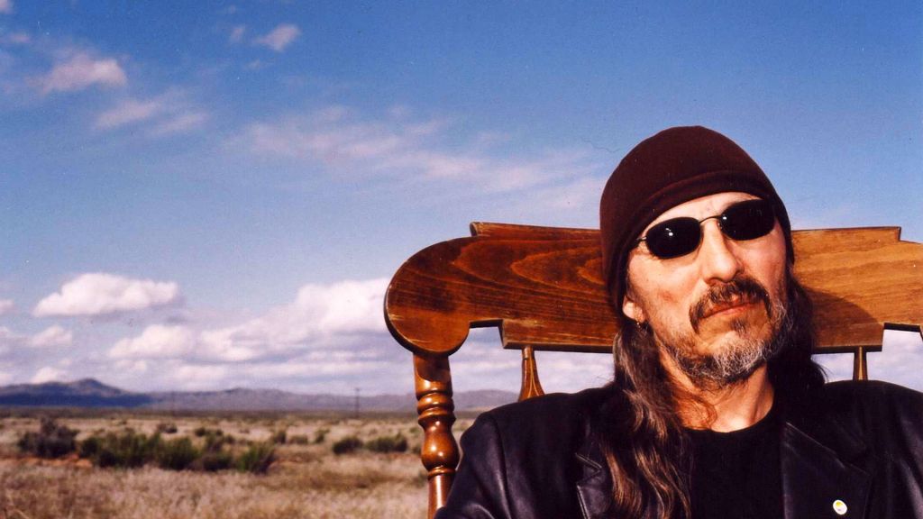 Activist and author John Trudell, sitting on a chair with wide open prairie in background