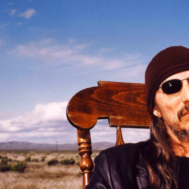 Activist and author John Trudell, sitting on a chair with wide open prairie in background