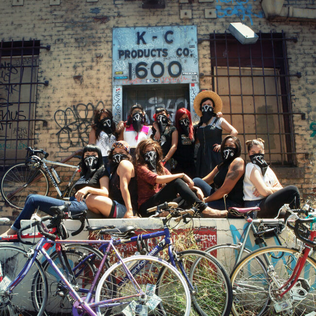 The Ovas bike brigade pose with bikes in front of a warehouse in East Los Angeles