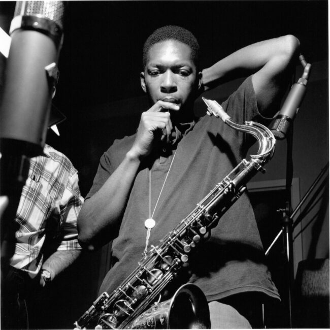 Young man with saxophone hanging from his while he looks down.