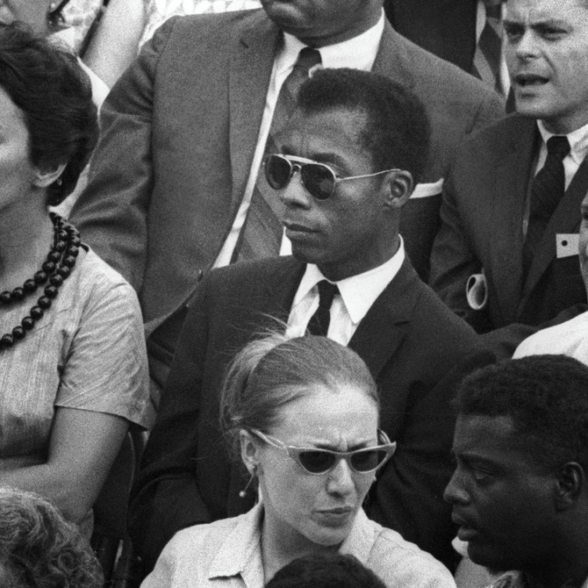 Malcom X sitting in a crowd looking off screen