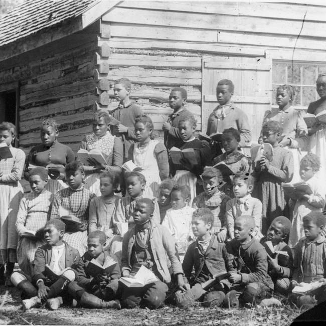 Group of children outside of school with books in hand looks colonial