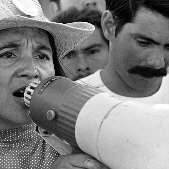 Dolores Huerta talking into megaphone while in a crowd