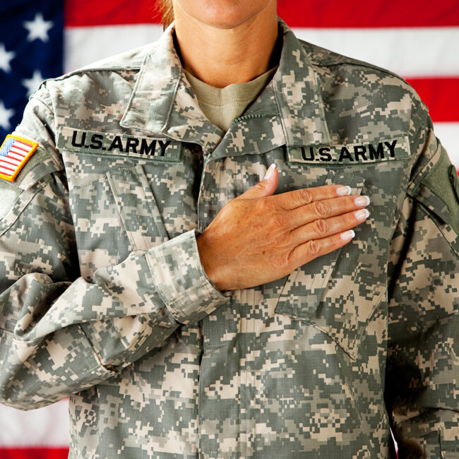Woman soldier in the army pledging allegiance with US flag behind her; image by By Sean Locke Photography and Shutterstock