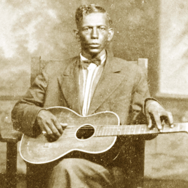 Man (Charley Patton) sitting for a portrait with a guitar in his lap