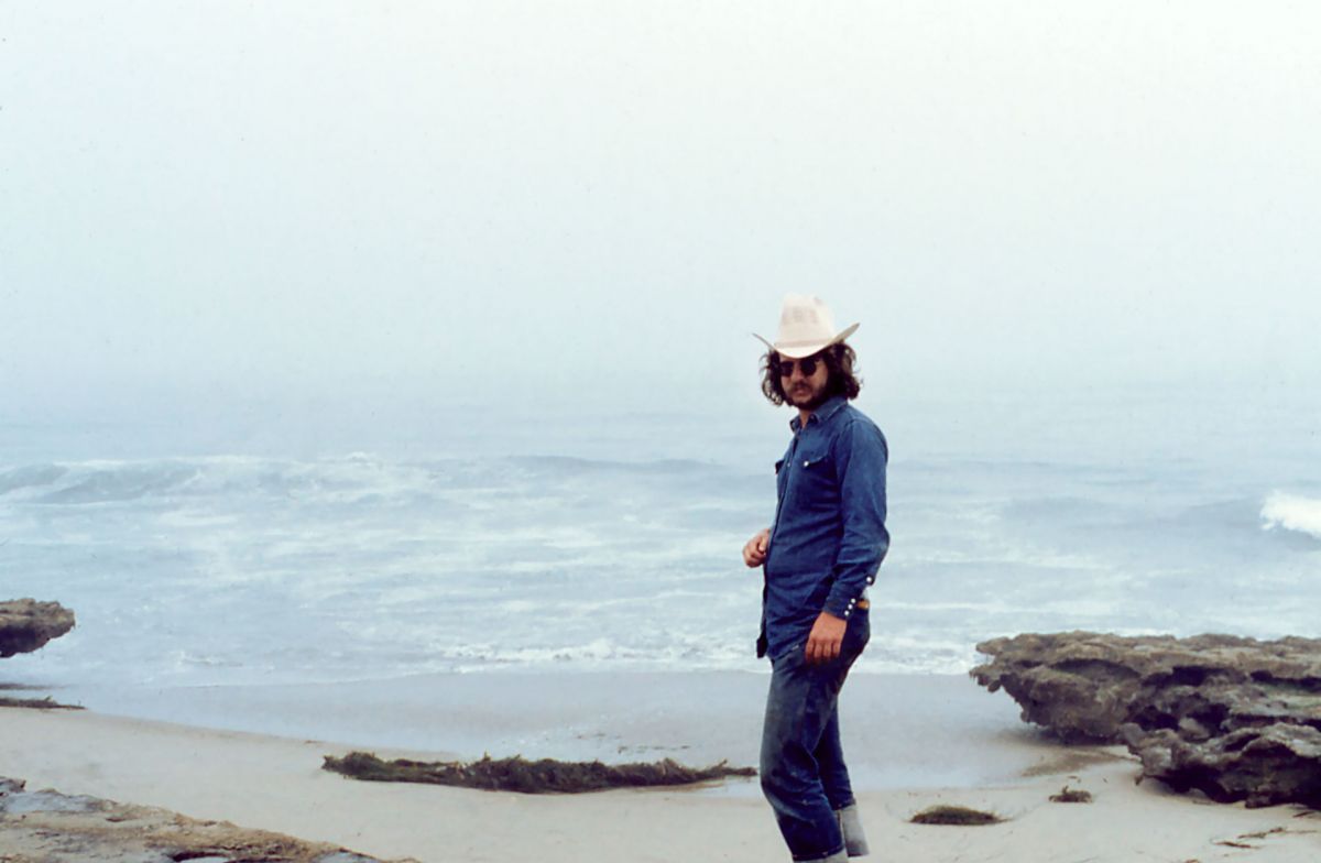 Archival shot of Jim Allison on a beach, wearing hat