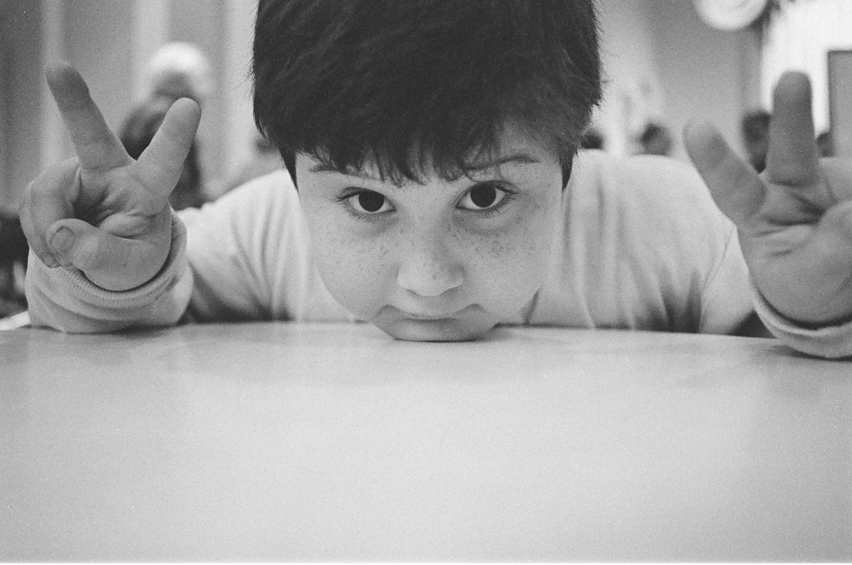 Young child with chin on table holding up peace signs