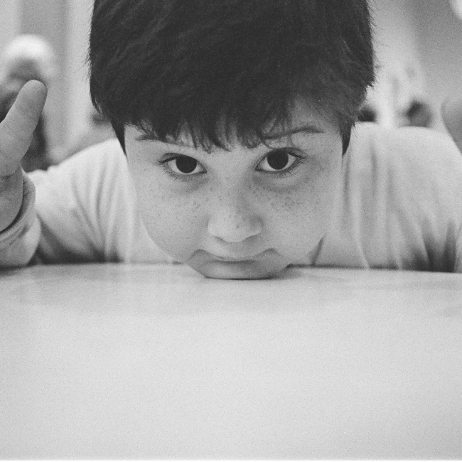 Young child with chin on table holding up peace signs