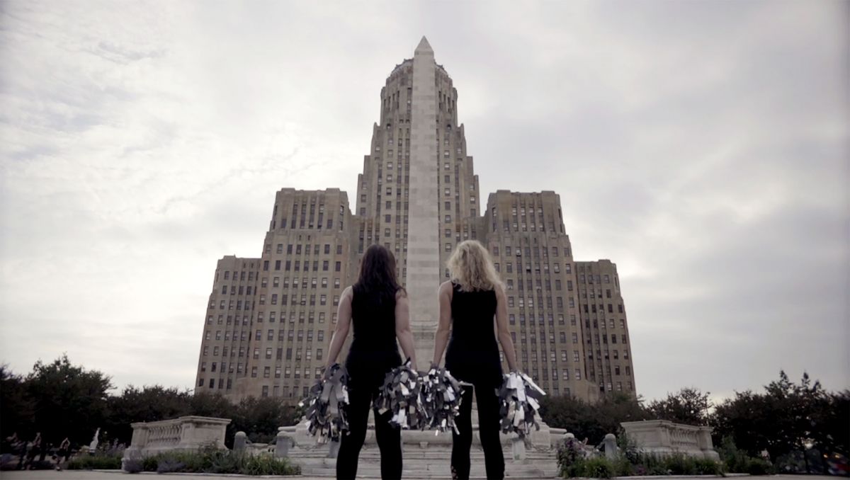 two women cheerleaders from a Woman's Work pose together as cheerleaders in front of courthouse