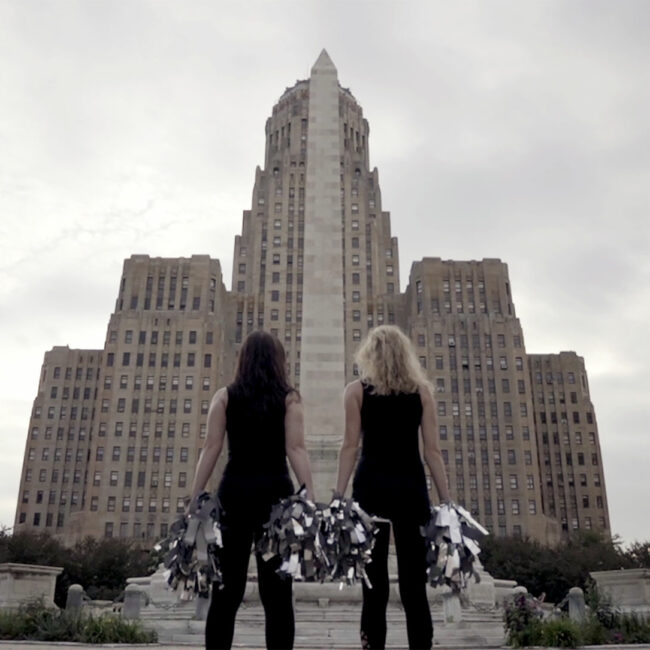 two women cheerleaders from a Woman's Work pose together as cheerleaders in front of courthouse