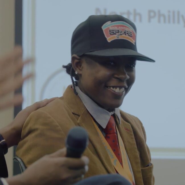 Woman (LaTonya Myers) in a San Antonio Spurs hat, celebrates a job offer