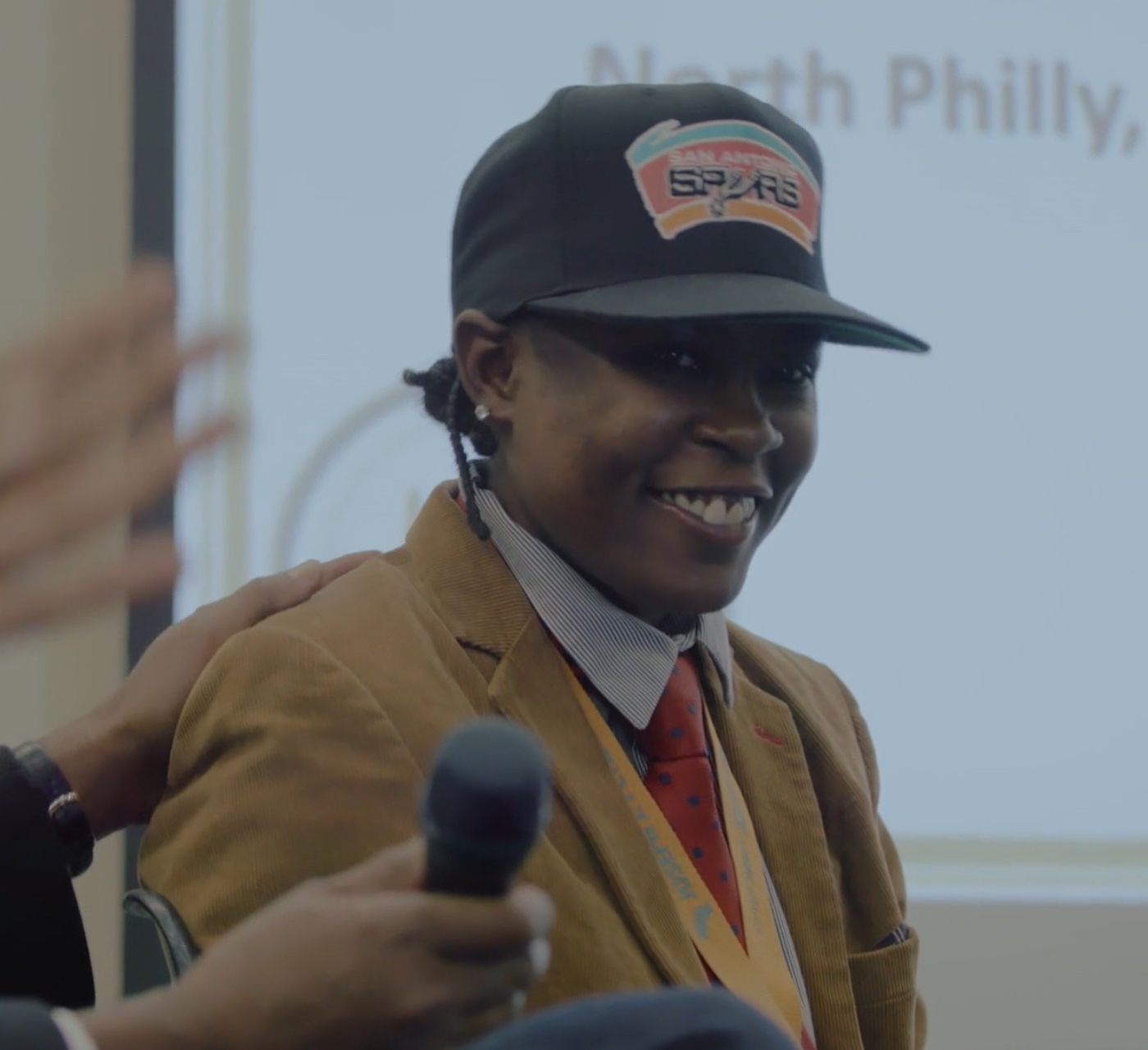 Woman (LaTonya Myers) in a San Antonio Spurs hat, celebrates a job offer