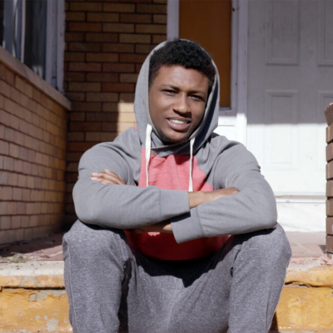 young man sits on the steps in Baltimore, in scene from Owned