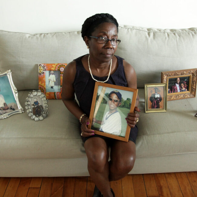 Woman sitting on couch surrounded by photos of her dead son