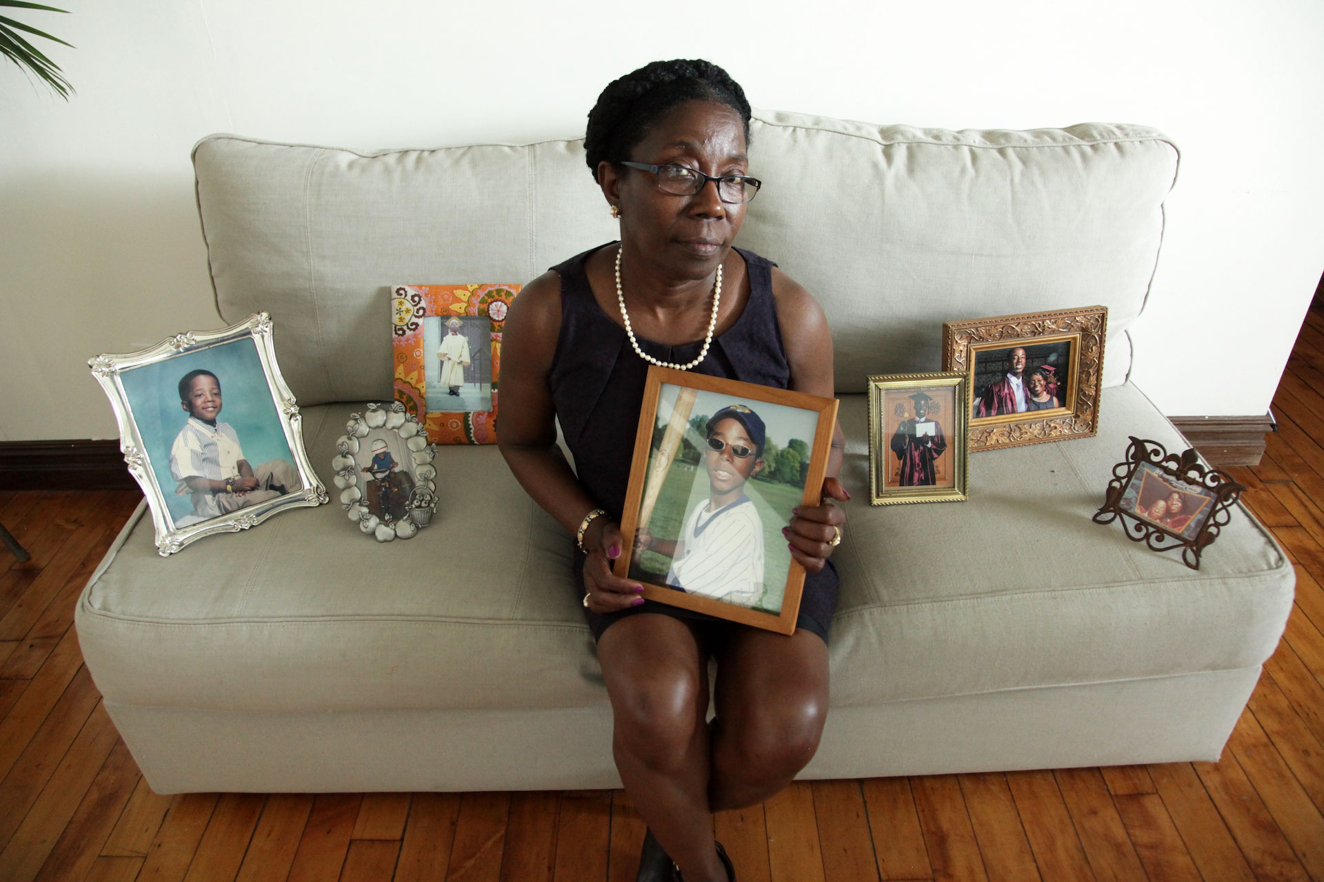 Woman sitting on couch surrounded by photos of her dead son