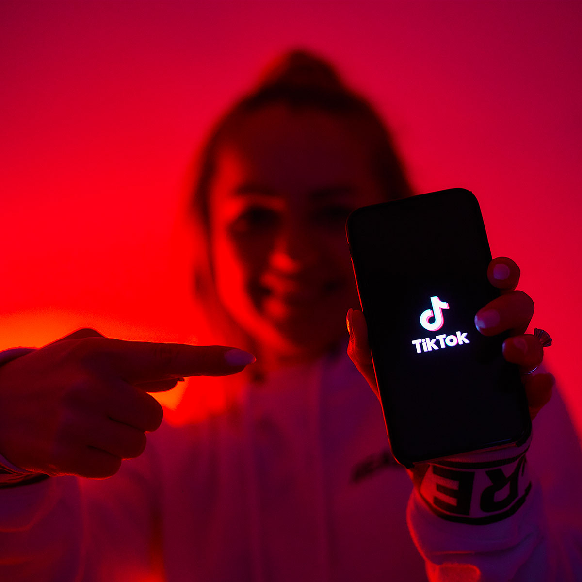 A girl in red background, darkened, tiktok promoting TikTok social network with a smartphone in hand.