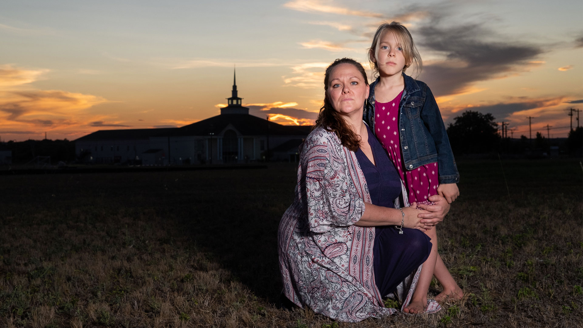 Kimberley and daughter Kai stand in front of a church at sunset