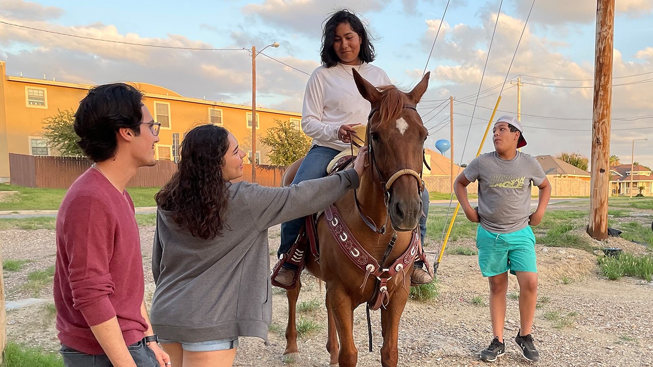 Three teens from the Texas/Mexico border chat with a fourth teen on a horse.