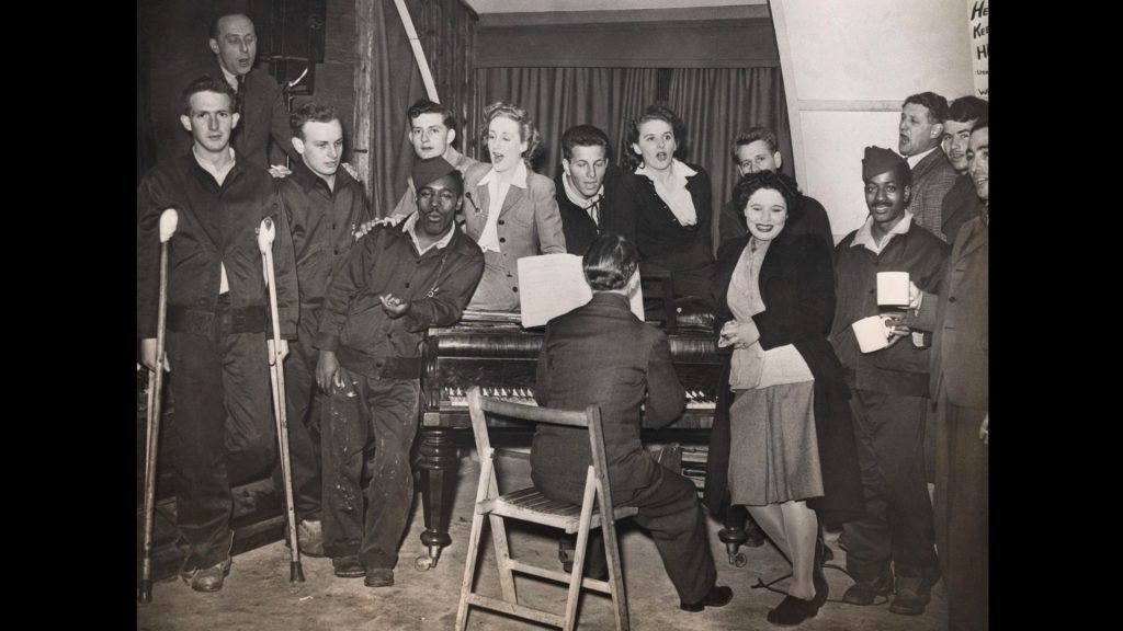 GIs and ENSA performers gathered around a piano, 1944