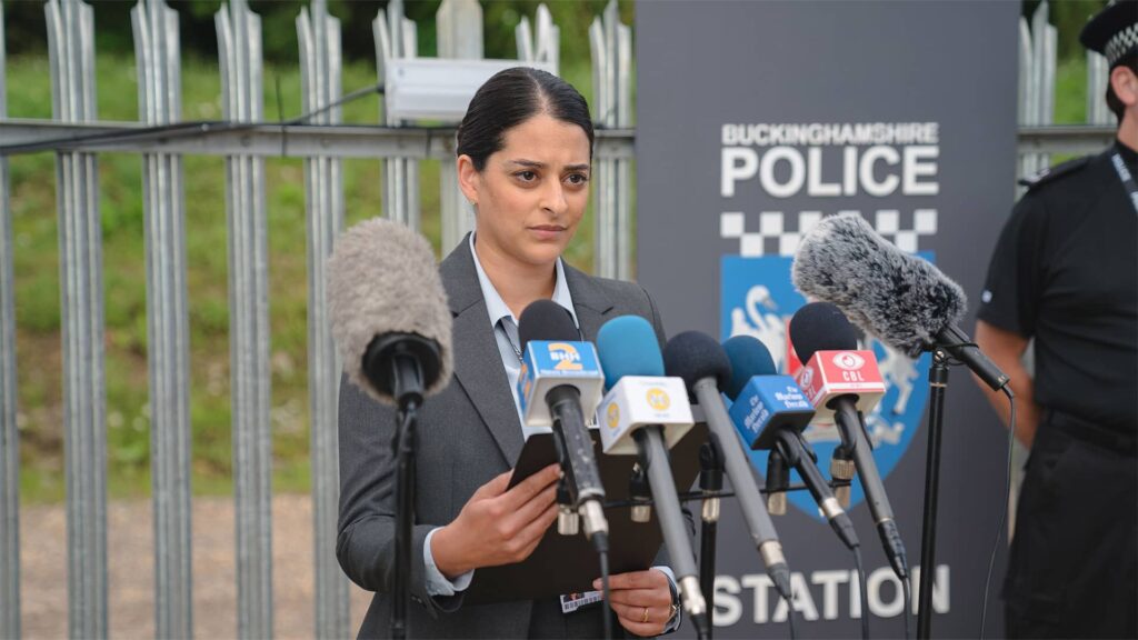 Natalie Dew as Tanika Malik speaking at a press conference in The Marlow Murder Club