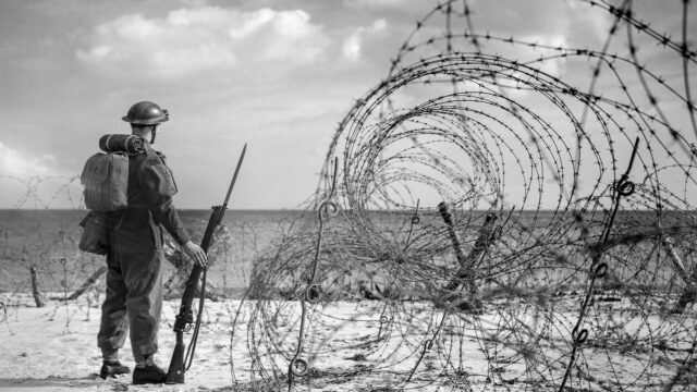 WW2 propaganda photo of British soldier standing guard on a beach in southern England, October 1940.