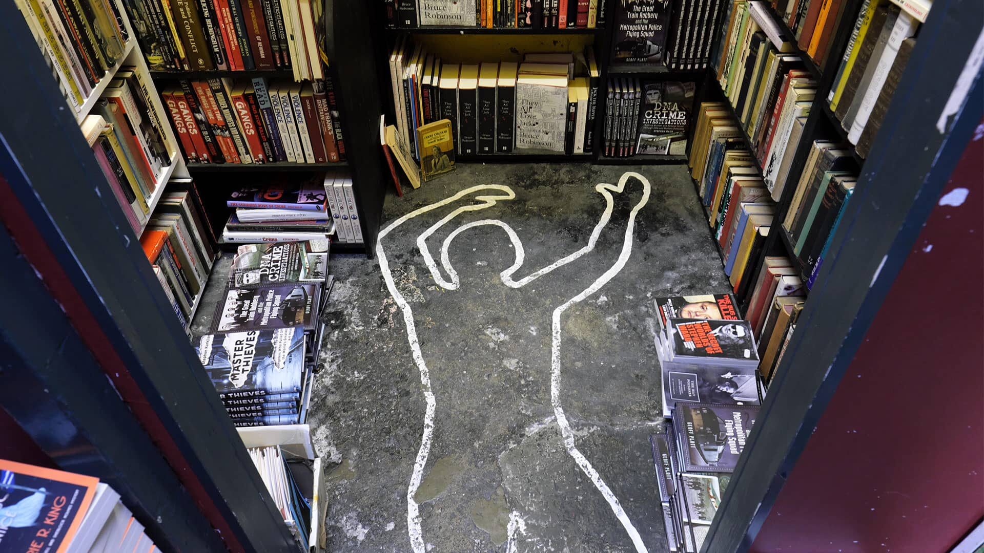 A chalked corpse outline is on the floor of a bookstore, surrounded by shelves filled with books