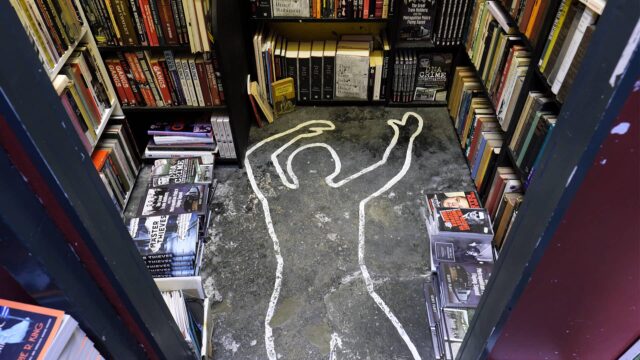 A chalked corpse outline is on the floor of a bookstore, surrounded by shelves filled with books