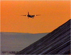 Airplane landing at airport in mountains, at sunrise